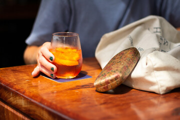 Person holding Red cocktail Aperol Spritz on wooden table in bar / restaurant with fresh orange....