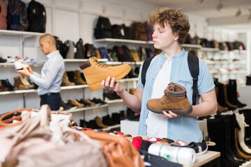 Obraz premium Interested teenage boy visiting shoe shop in search of comfortable spring and autumn shoes .