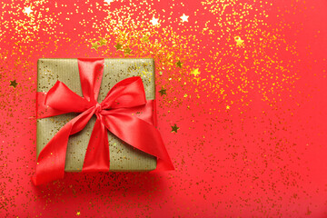 Beautiful Christmas gift and golden confetti on red background