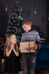 Fototapeta na wymiar charming blonde little boy and girl near christmas tree. brother and sister celebrating new year.