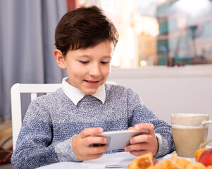 Teenager plays on smartphone in kitchen interior. High quality photo