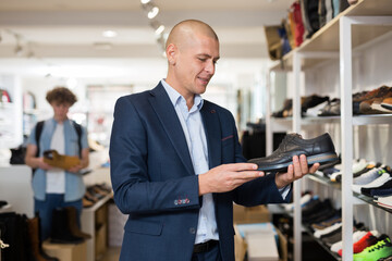 Fototapeta na wymiar Smiling young man wearing in suit looking for comfortable classic shoes in shoe store.