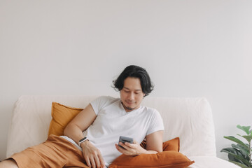 Freelance long hair Asian man sit on the sofa and use application smartphone.