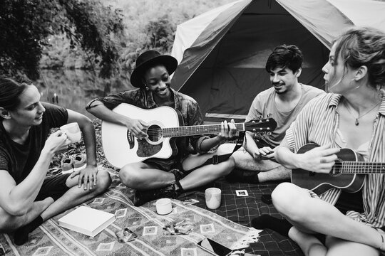 Group of young adult friends in camp site playing guitar and uke