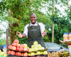 Happy African male trader or vendor standing at his fruit stall in a market place