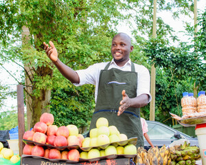 Happy African male trader or food vendor standing at his fruit stall in a market place