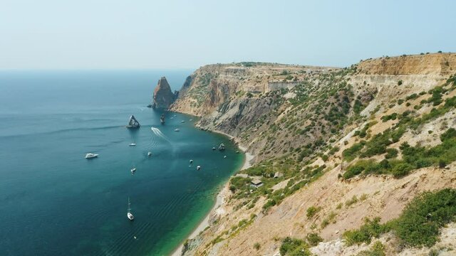 Aerial view of calm azure sea and volcanic rocky cliffs of Mys Fiolent. Pleasure trip boats moored in the bay. Nature summer ocean sea beach background. Holiday, vacation and travel concept