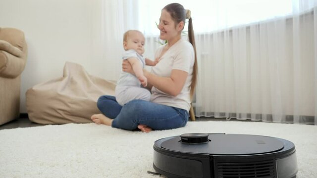 Robot vacuum cleaner helping woman doing chores while she spend time with baby son. Concept of hygiene, household gadgets and robots at modern life.