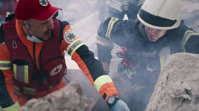 Diverse emergency service worker and medical practitioner examining and discussing remains of demolished building after earthquake
