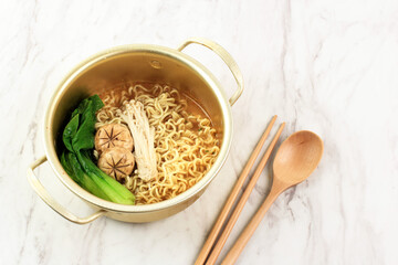 Korean Style Instant Noodle, Ramyeon or Ramyun with Spicy Flavour Topped with Half Boiled Egg, Enoki Mushroom, and Kimchi in a Gold Korean Bowl above Black Wooden Table, Isolated