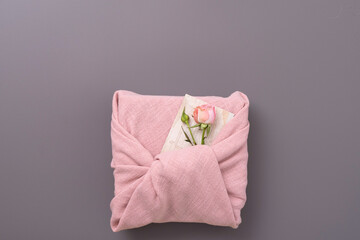 a beautiful gift wrapped in pink cotton fabric and decorated with a flower and a postcard, top view
