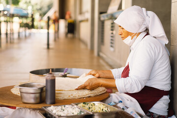Turkish Woman making Tortillas on a wooden rustic table. A cook prepares tortillas with different fillings at a street in the summer.