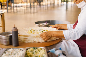 Turkish Woman making Tortillas on a wooden rustic table. A cook prepares tortillas with different fillings at a street in the summer.