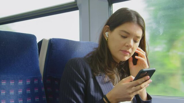 Businesswoman with earbuds listening to music commuting to work on train looking at mobile phone - shot in slow motion