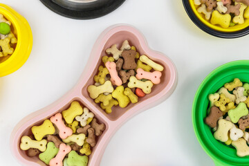 Pink bowl with snacks for dog on white background. Dog food and multicolored bones.