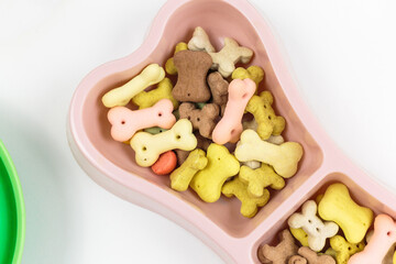 Pink bowl with snacks for dog on white background. Dog food and multicolored bones.