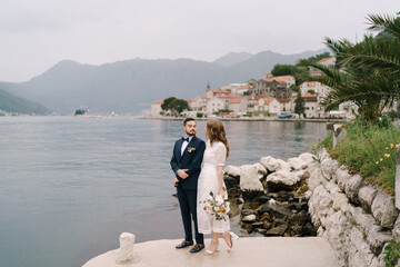 Bride and groom stand on the pier by the water against the background of Perast. Montenegro