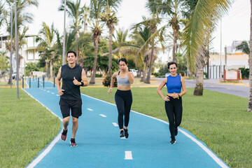 Fototapeta premium Three hispanic young adults running at a public park. Front view