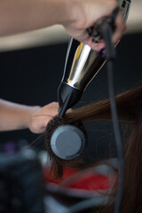hands of a stylist using a blow dryer and a comb on the client's hair
