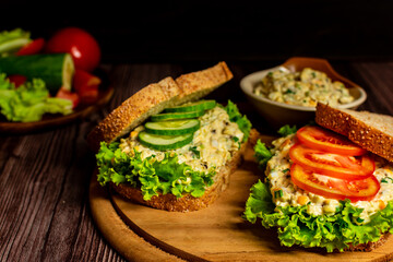 Homemade egg salad sandwich with wholewheat bun,cucumber, tomatoes,lettuce,egg,and cream cheese.  Rustic style. Selective Focus. Top view. Copy space. No.09