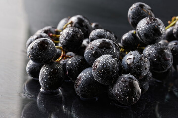 Black grapes covered with moisture droplets on a reflective surface. Macro. Selective focusing