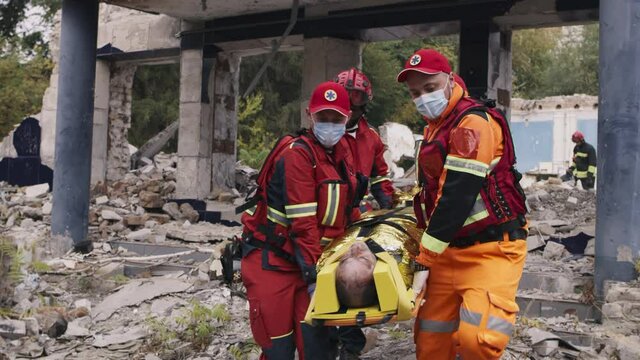 Tracking shot of multiracial men in paramedic uniform carrying survival and walking towards emergency vehicle during rescue mission after earthquake