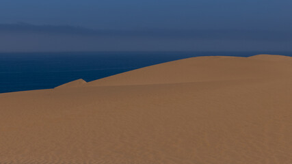 Fototapeta na wymiar Eine grosse Sanddüne vor dem blauen Atlantik, über dem Dunst aufsteigt