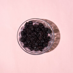 Raisins in a glass container with pink background