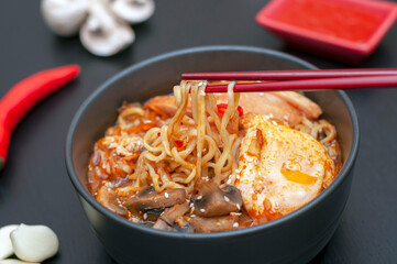 chopsticks hold Ramen - a national, popular dish of traditional Korean cuisine. Asian soup with noodles, chicken breast, egg, mushrooms, broth, hot sauce and spices.