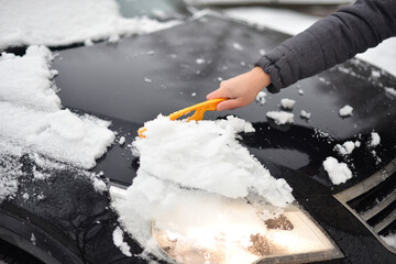  A hand sweeps snow from the hood of the car.