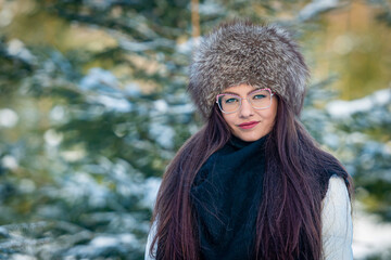 cheerful lady in glasses and winter clothes posing with joy outside in the snow forest