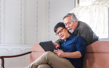 Obraz premium Adult son and senior asian father using tablet smartphone in living room, Happy family concepts