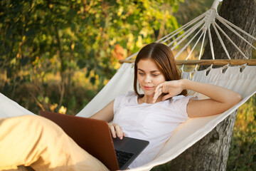 women outdoors lies in a hammock with a laptop freelance internet