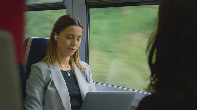 Businesswoman with earbuds listening to music commuting to work on train working on laptop - shot in slow motion