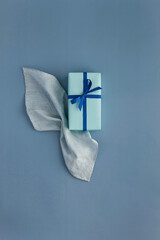 A gift box wrapped in blue wrapping paper with blue ribbon on blue background