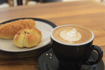 A glass of coffee latte with floral motifs on the coffee surface side by side with pastries on the table
