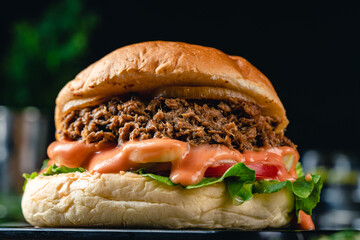 Tasty grilled tuna burger or sandwich with lettuce, tomato, onion rig and mayonnaise served on wooden table. dark mood.