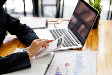 Close up a Business woman using calculator and laptop for doing math finance on a wooden desk, tax, accounting, statistics, and analytical research concept