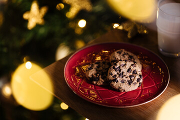 Cookies and warm milk left for Santa. Chocolate chip cookies and glass of milk in front of Christmas tree that is left blurred in background