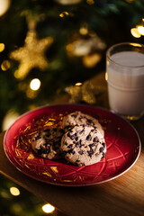 Cookies and warm milk left for Santa. Chocolate chip cookies and glass of milk in front of Christmas tree that is left blurred in background