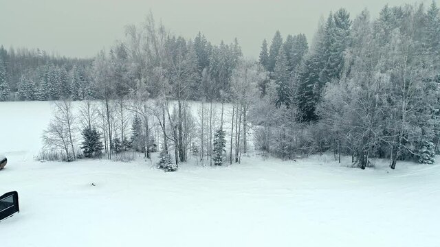 Aerial flight during falling snowflakes during white winter day in Wilderness - Wooden House and Barell Sauna in Nature