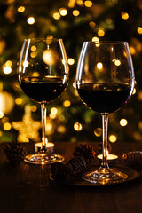 Two glasses of red wine in front of Christmas tree and lights in blurry background, festive atmosphere