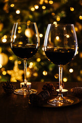 Two glasses of red wine in front of Christmas tree and lights in blurry background, festive atmosphere