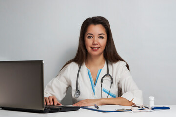 Fototapeta na wymiar Young woman doctor sitting at office desk and working on laptop
