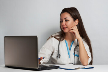Young woman doctor sitting at office desk and working on laptop