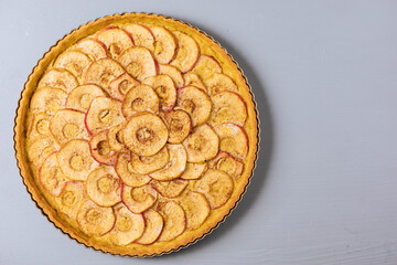 Top view of Classic french apple tart on a grey background with apples and cinnamon sticks