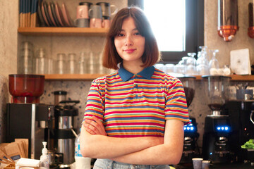 A cute bar waitress is standing behind the bar counter with crossed arms and smiling.