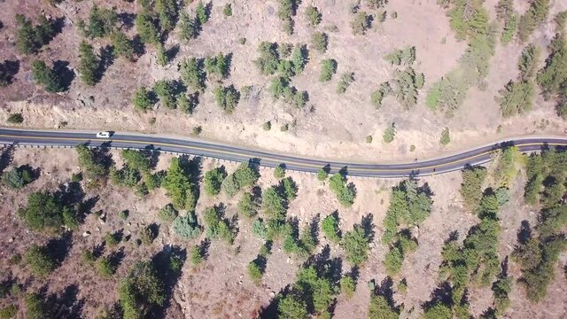 A winding road in the mid west USA with a car driving along with it. A very dry video with baren life.