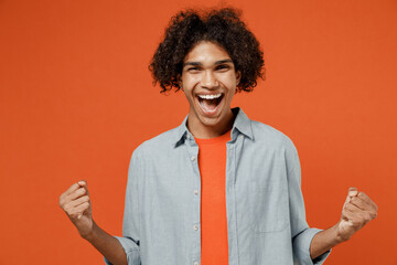 Young overjoyed fun student black man 50s wearing blue shirt t-shirt look camera do winner gesture scream say yes isolated on plain orange color background studio portrait. People lifestyle concept.