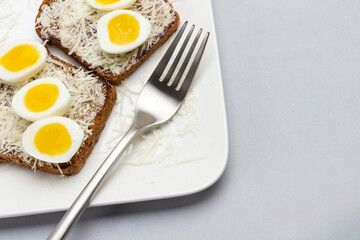 Toast with grated cheese and boiled quail eggs, fork on white plate.